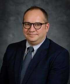 Man in dark suit with blue tie, wearing dark glasses