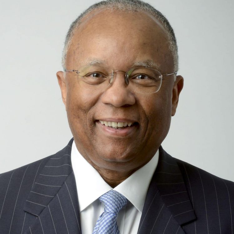 Man in charcoal striped suit with white shirt and light blue tie. Man is wearing glasses.