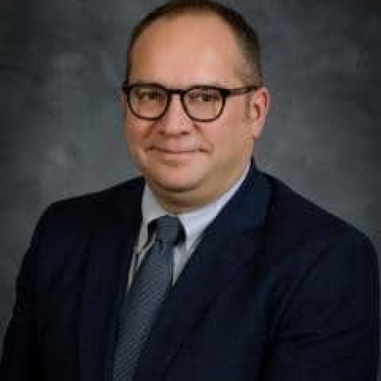 Man in dark suit with blue tie, wearing dark glasses